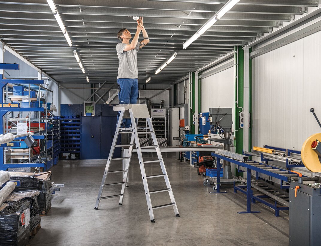 Volle Sicherheit bei der Arbeit bietet die neu entwickelte TRBS-konforme Sicherheits-Stufen-Stehleiter mit integrierter Stützblende an den beiden obersten Stufen. | © MUNK GmbH